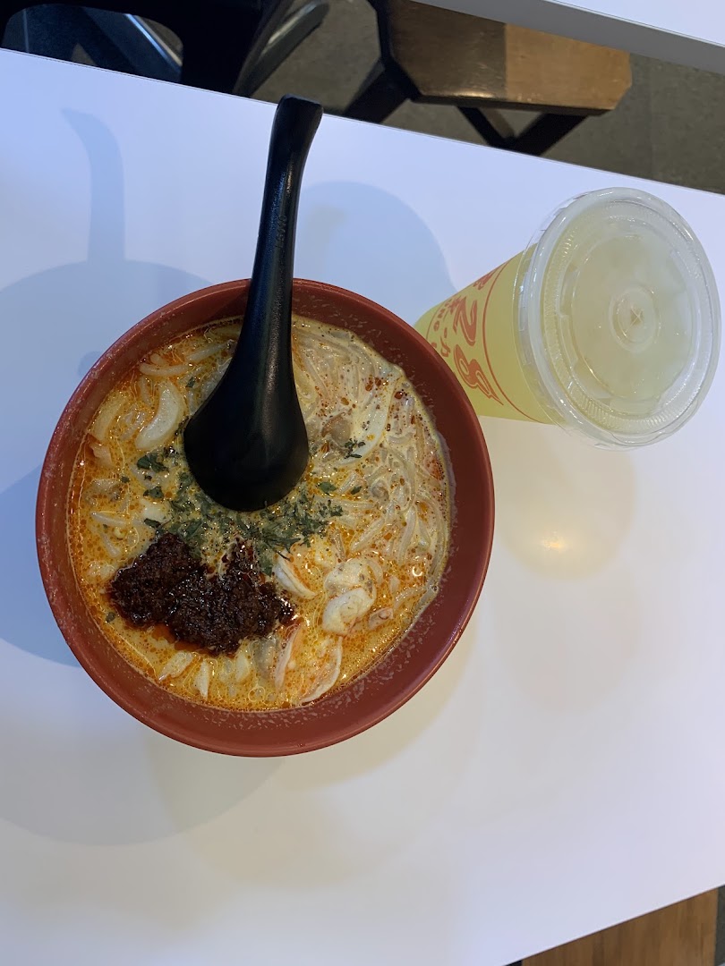 A vibrant bowl of Katong Laksa with a side drink, showcasing the rich broth and fresh ingredients.
