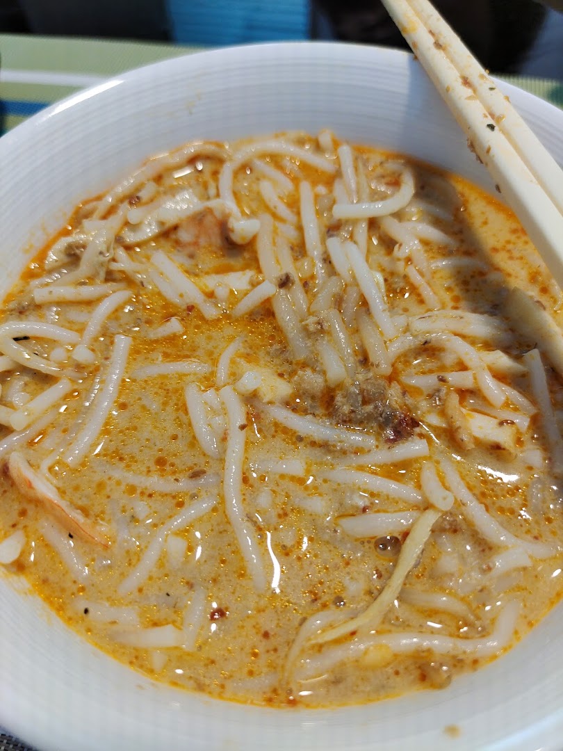A close-up of a delicious bowl of Katong Laksa with thick rice noodles and rich broth.
