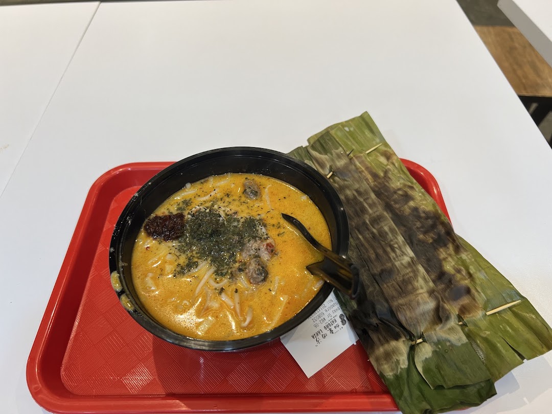 A vibrant bowl of Katong Laksa with grilled otah on a red tray.
