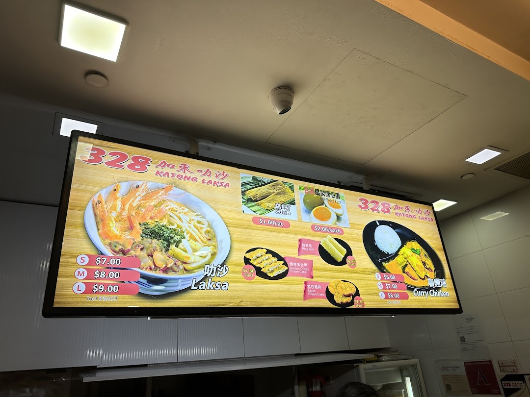 A bright digital menu board showcasing 328 Katong Laksa's signature dishes and side orders with prices.
