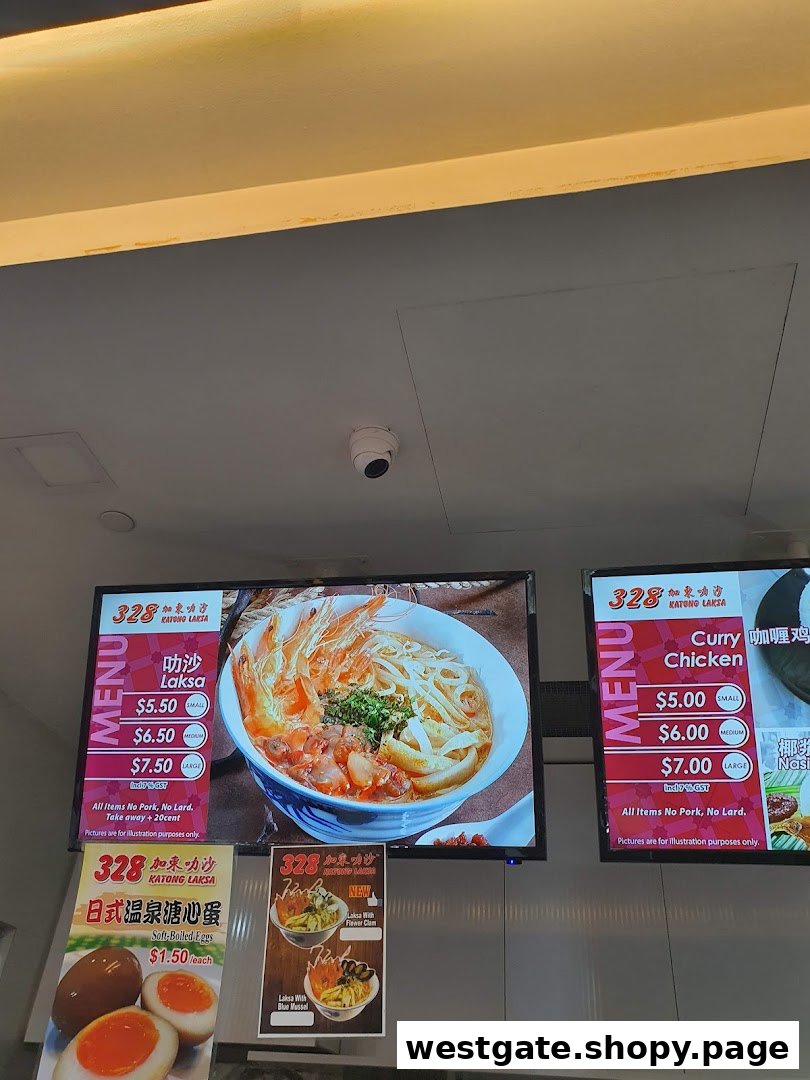 Digital menu boards and signs displaying Laksa, Curry Chicken, and side dishes with prices.