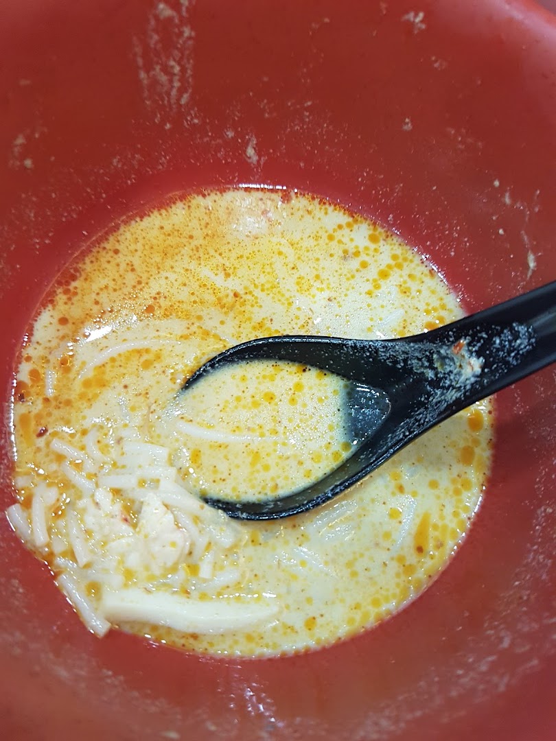 A close-up of a bowl of creamy laksa with noodles and a spoon.