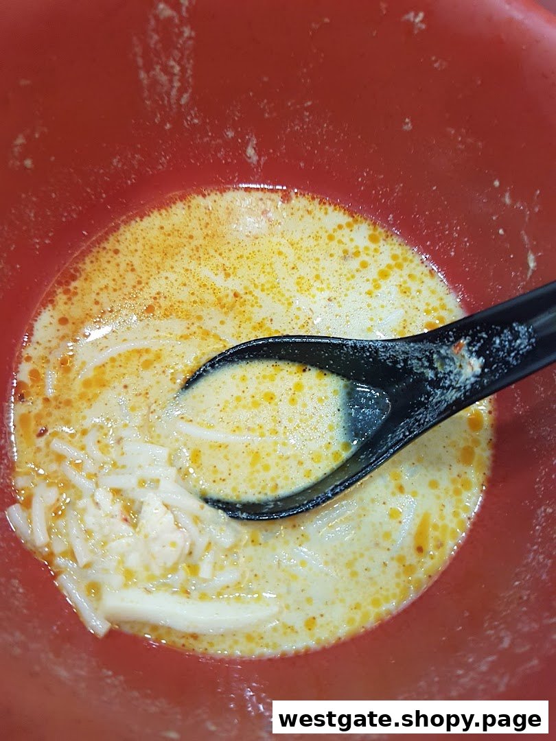 A close-up of a bowl of creamy laksa with noodles and a spoon.