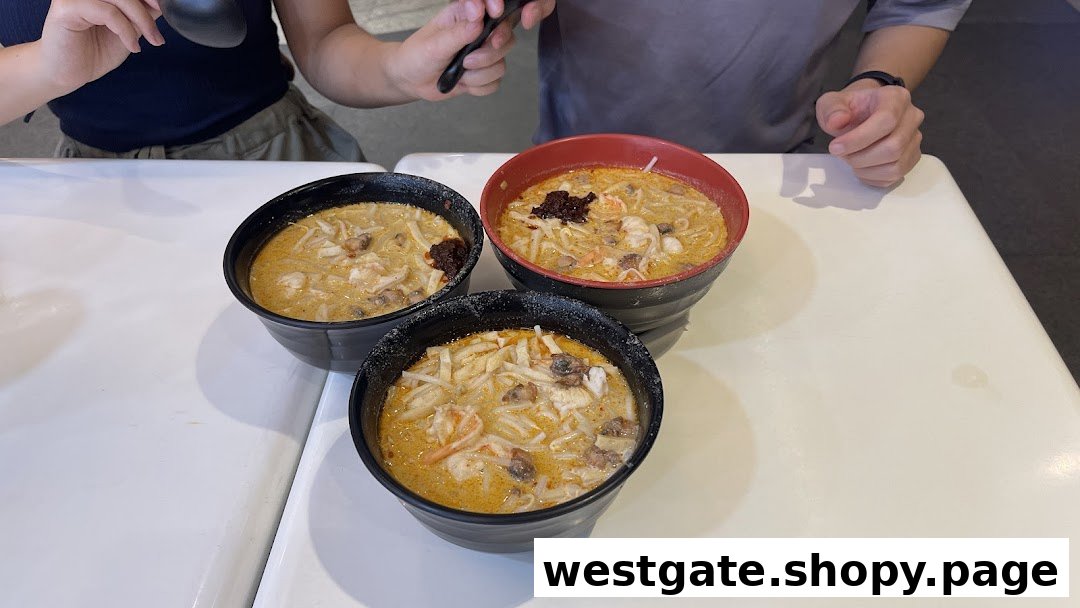 Three bowls of authentic Katong Laksa with rich broth and fresh ingredients on a white table.
