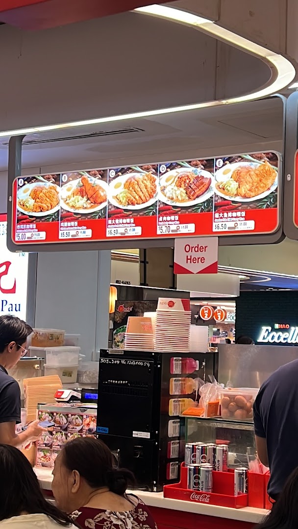 A digital menu board displaying various curry rice dishes with prices above a bustling food stall counter.