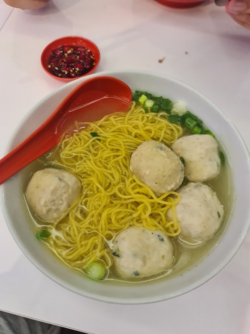 A close-up of a bowl of Teochew fishball noodles with a side of chili sauce.