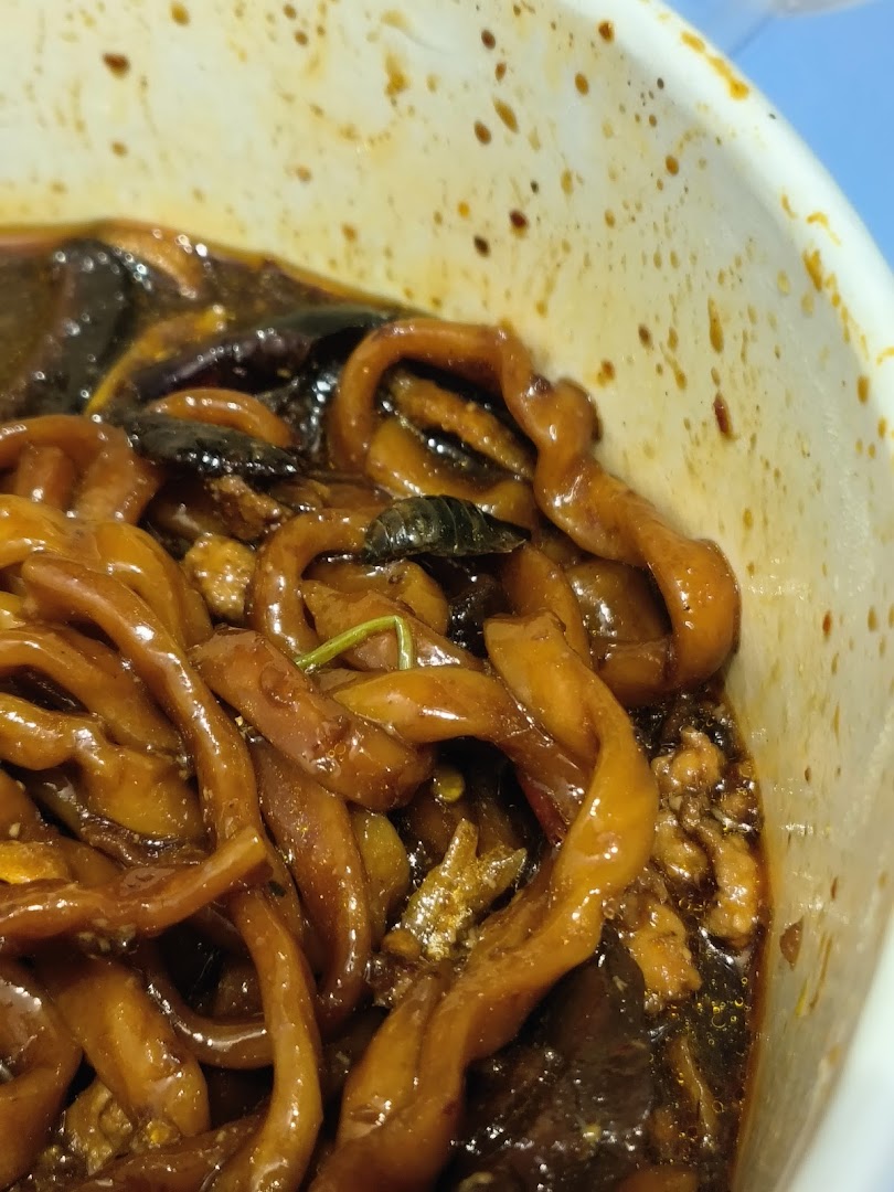 A close-up view of dark sauced noodles in a white bowl, showcasing the texture.