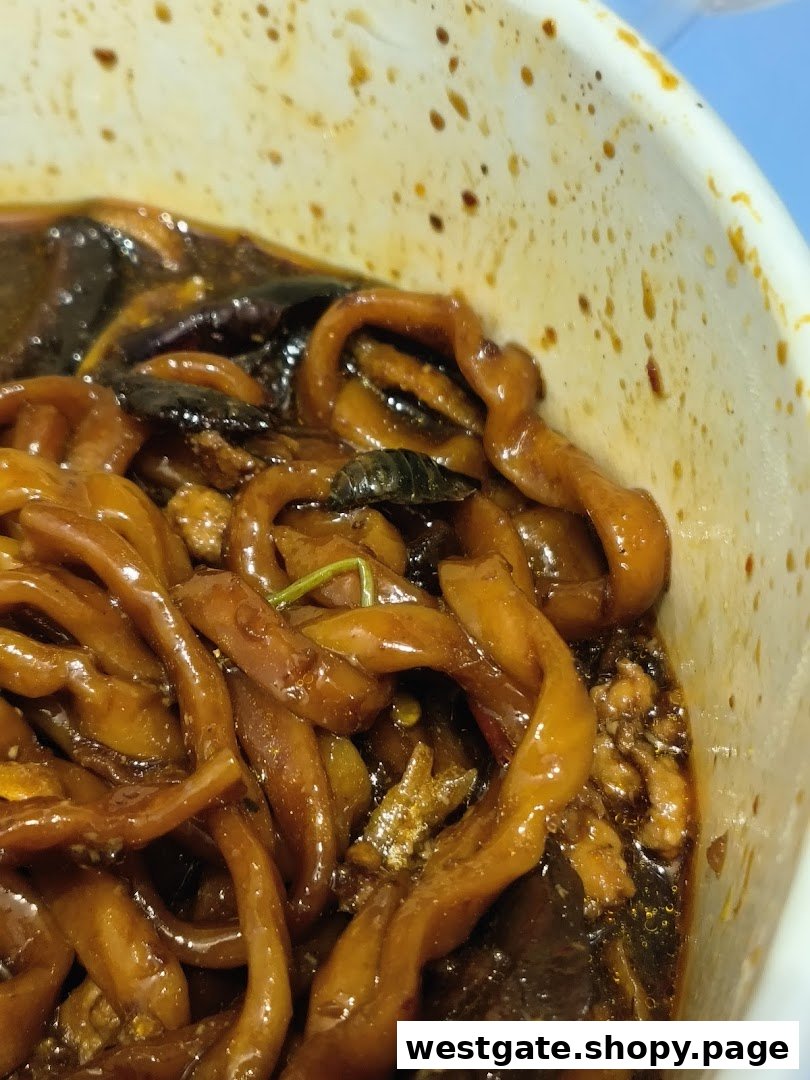 A close-up view of dark sauced noodles in a white bowl, showcasing the texture.