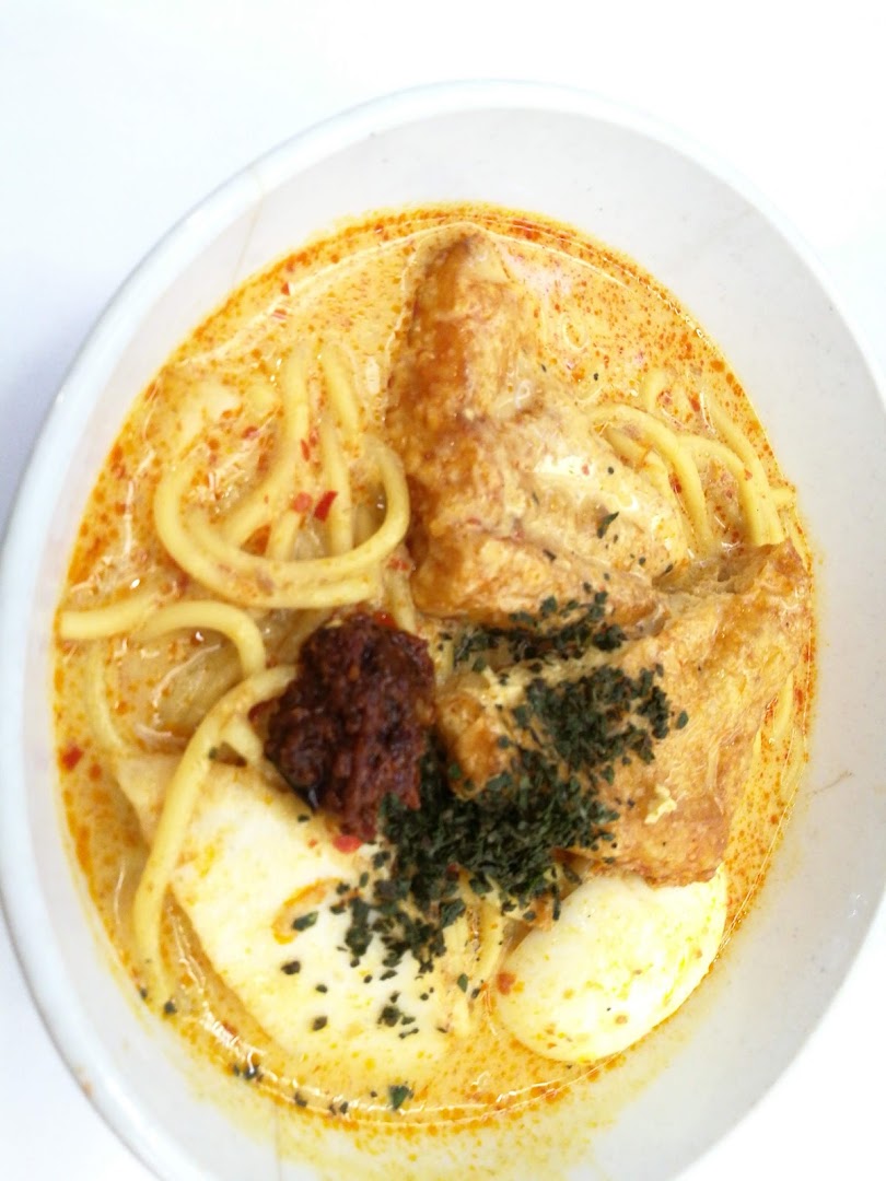 A vibrant bowl of curry noodles with tofu, egg, and chili paste, garnished with herbs.