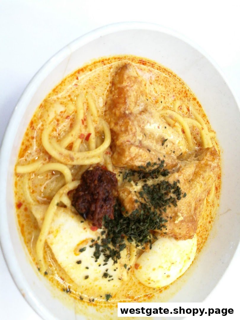 A vibrant bowl of curry noodles with tofu, egg, and chili paste, garnished with herbs.