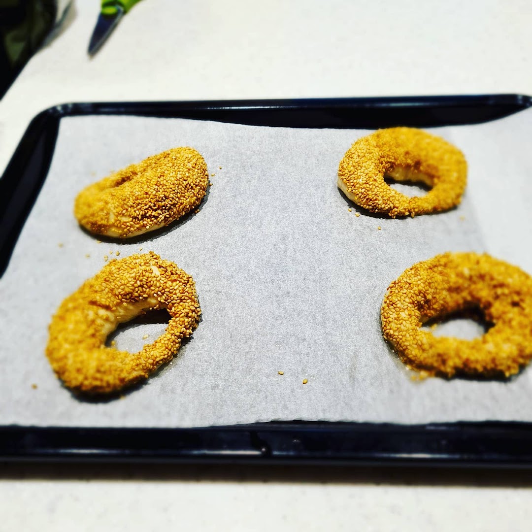Four sesame-covered dough rings on a baking sheet, ready for baking.