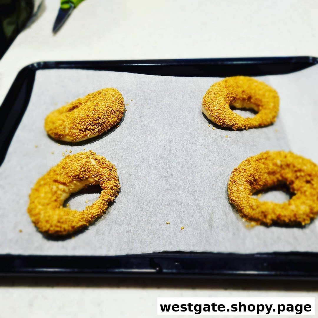 Four sesame-covered dough rings on a baking sheet, ready for baking.