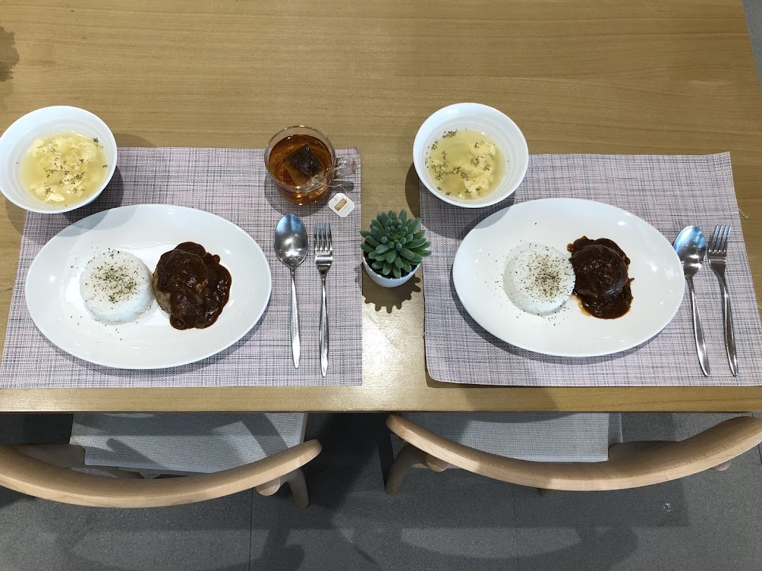 Two plates of hamburger steak with rice, soup, and tea, set on a wooden table.
