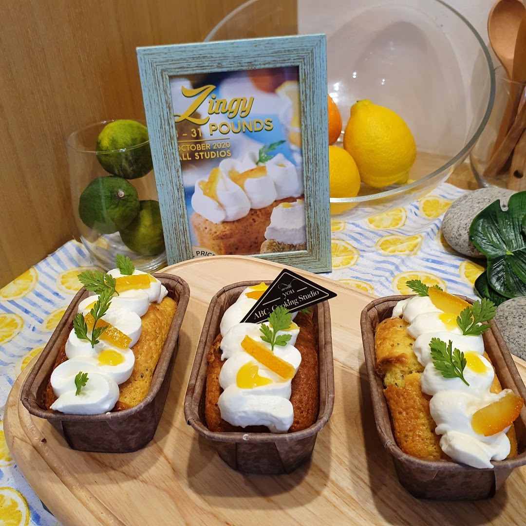 Three lemon poppy seed loaves with cream and candied peel on a display, featuring a 'Zingy' poster.