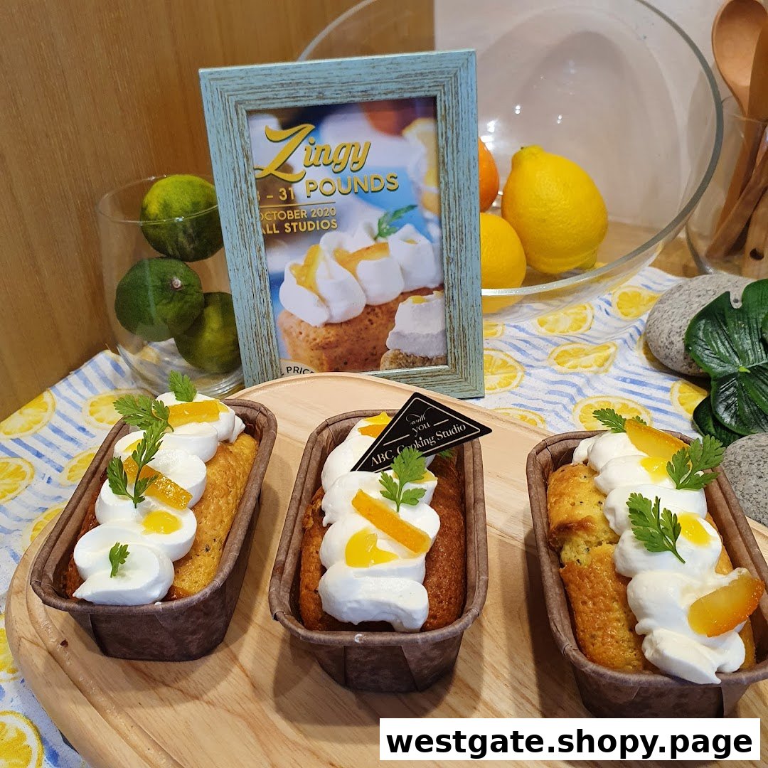 Three lemon poppy seed loaves with cream and candied peel on a display, featuring a 'Zingy' poster.