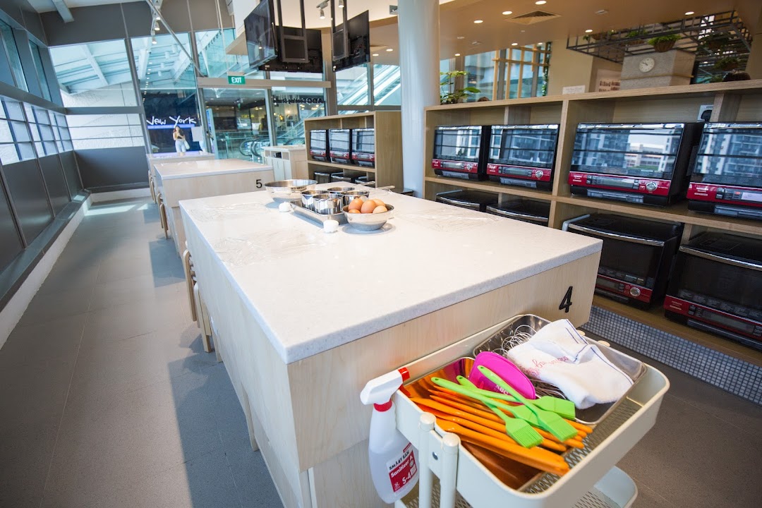 A bright, modern cooking studio interior with workstations, baking ingredients, and ovens.