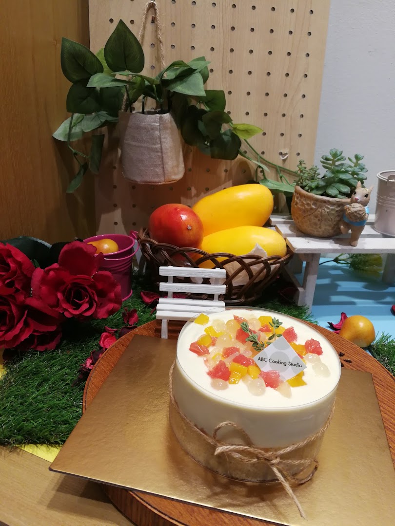 A beautifully decorated cake with fruit toppings, displayed amidst decorative elements at ABC Cooking Studio.
