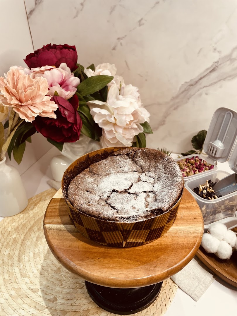 A freshly baked chocolate cake, dusted with powdered sugar, displayed on a wooden stand.