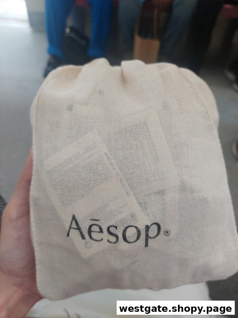 A hand holds a natural fabric drawstring bag featuring the Aesop logo, likely containing skincare products.