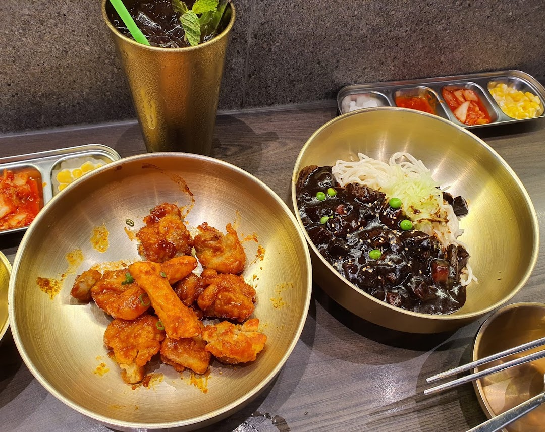 A close-up of delicious Korean dishes including fried chicken, black bean noodles, and banchan served in golden bowls.
