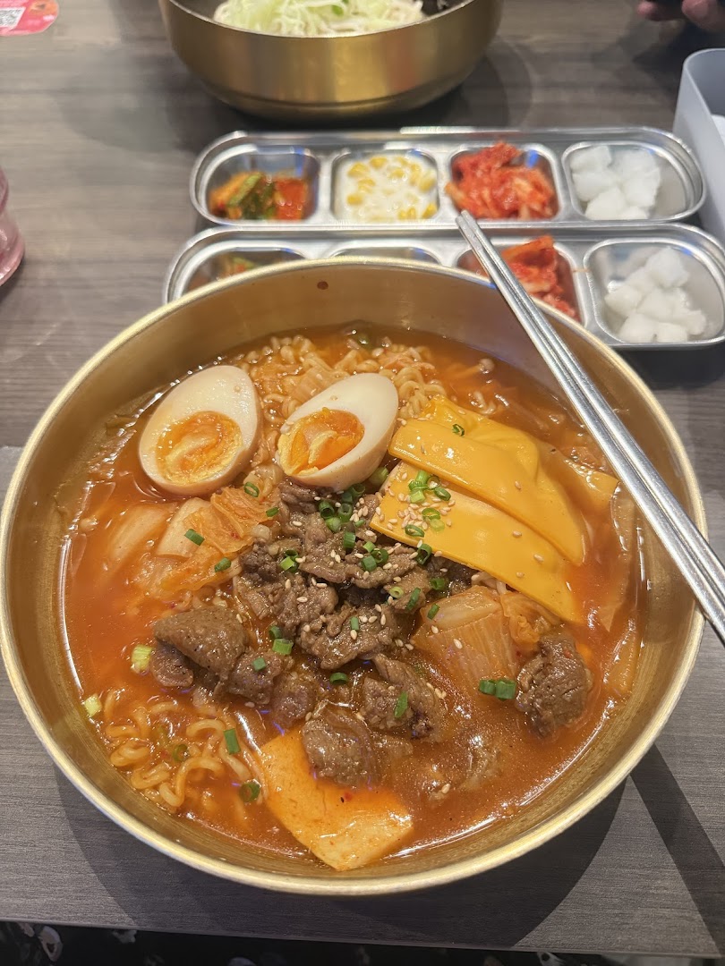 A vibrant bowl of Korean ramen with beef, egg, cheese, and kimchi, served with banchan.