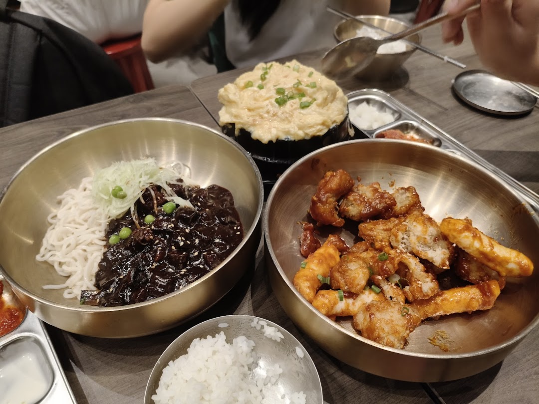 A table spread with various Korean dishes including Jajangmyeon, fried chicken, and steamed egg.