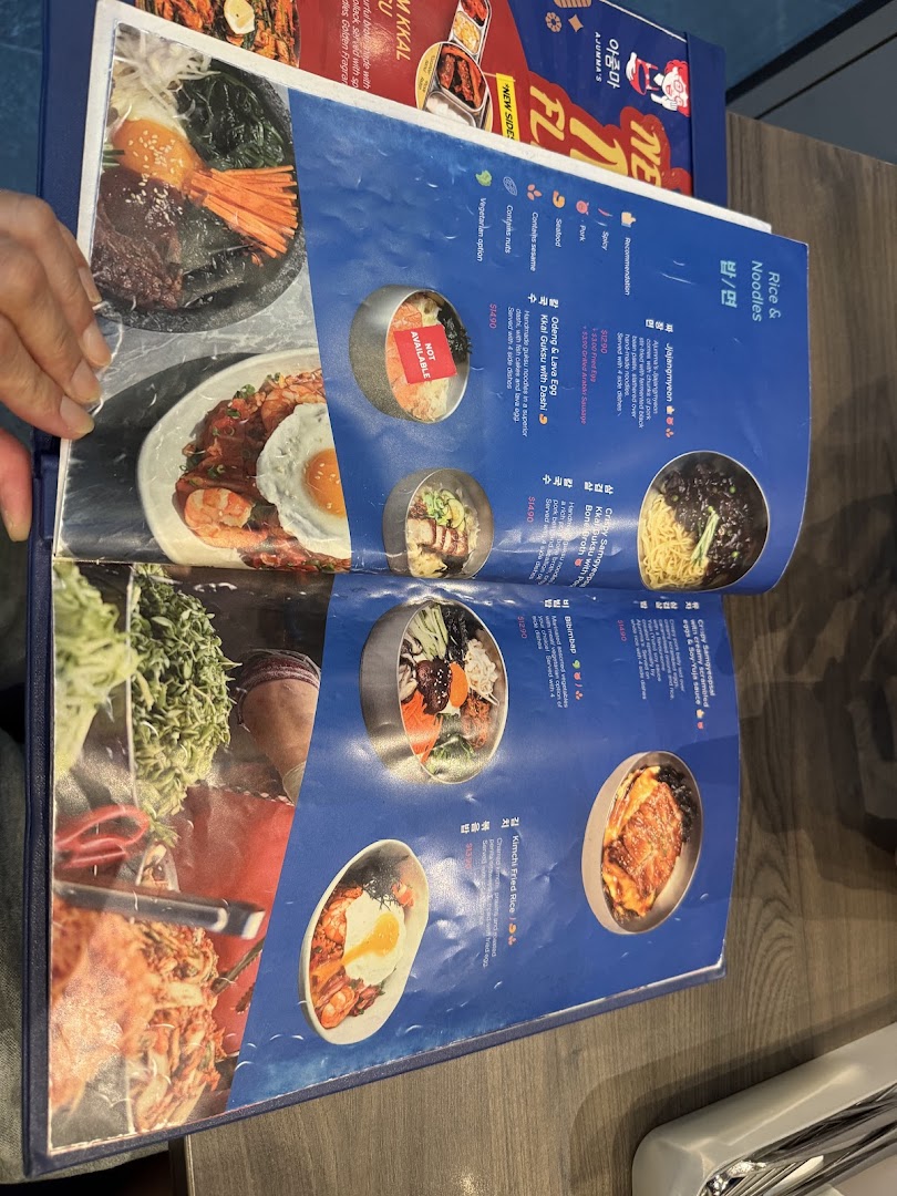 An open menu from Ajummas showcasing Korean rice and noodle dishes with prices and descriptions.