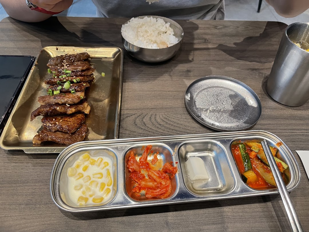 A delicious Korean meal featuring grilled meat, rice, and an assortment of traditional banchan on a wooden table.