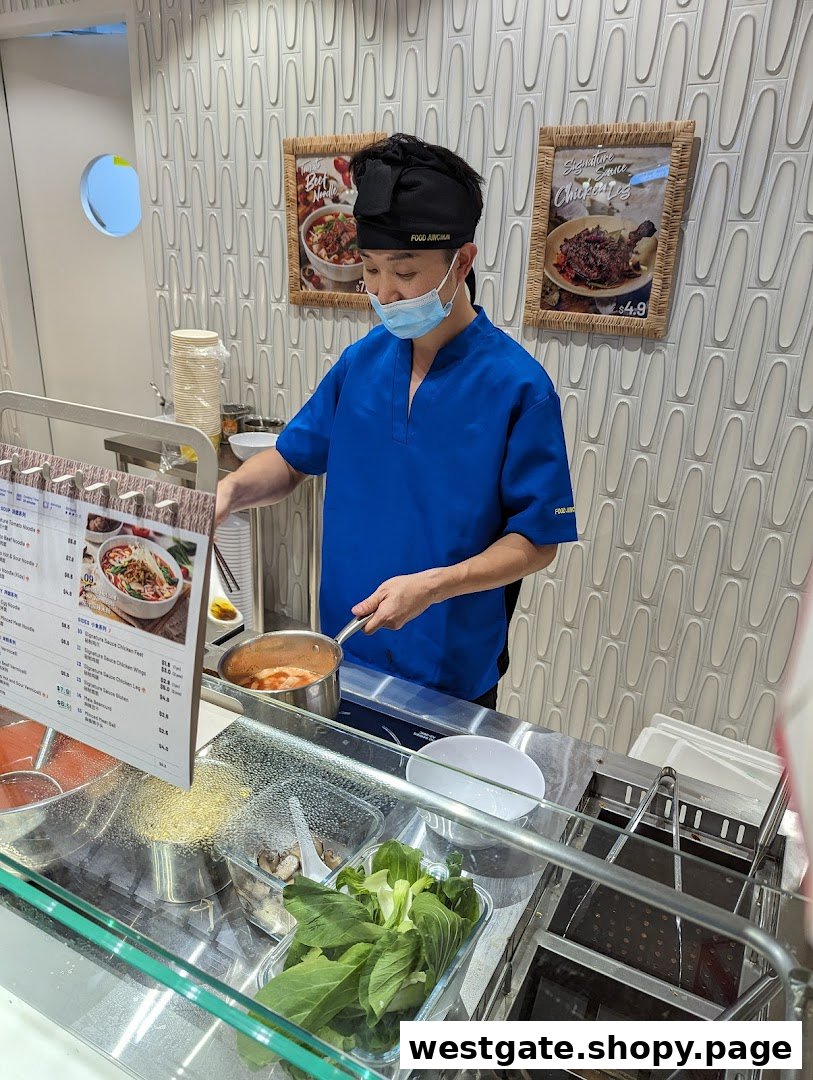 A chef in a blue uniform prepares a fresh noodle dish at the counter of Ali Tomato Soup Noodle.