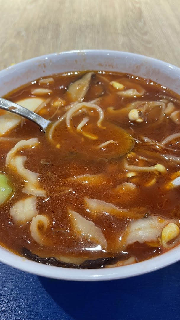 A close-up of a vibrant red tomato soup noodle dish with various ingredients.