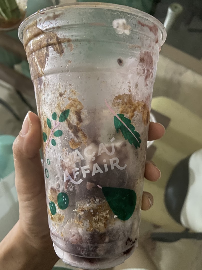 A hand holds a clear cup from 'An Açaí Affair' with açaí and topping remnants.