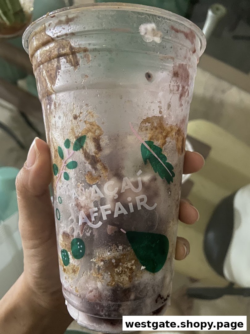 A hand holds a clear cup from 'An Açaí Affair' with açaí and topping remnants.