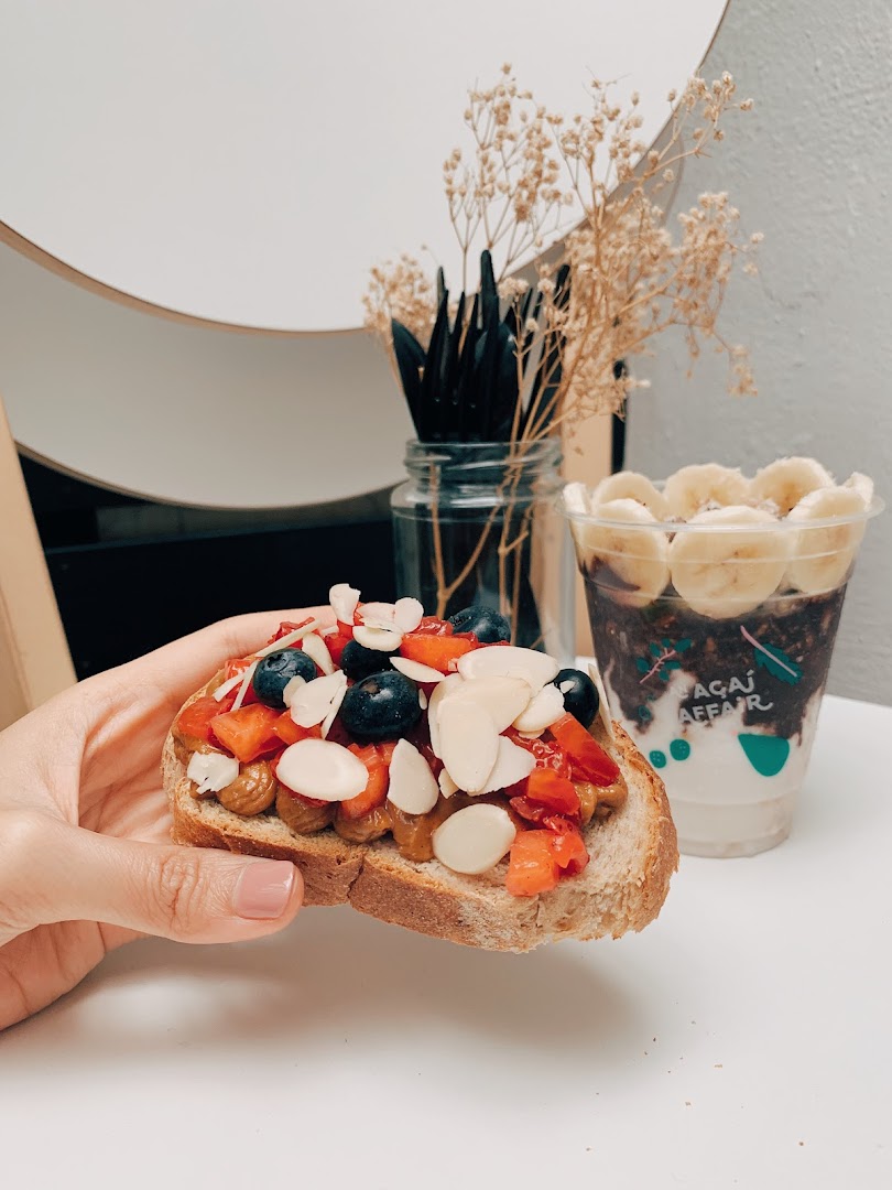 A hand holds a berry-topped toast next to an açaí bowl, showcasing fresh, healthy options.