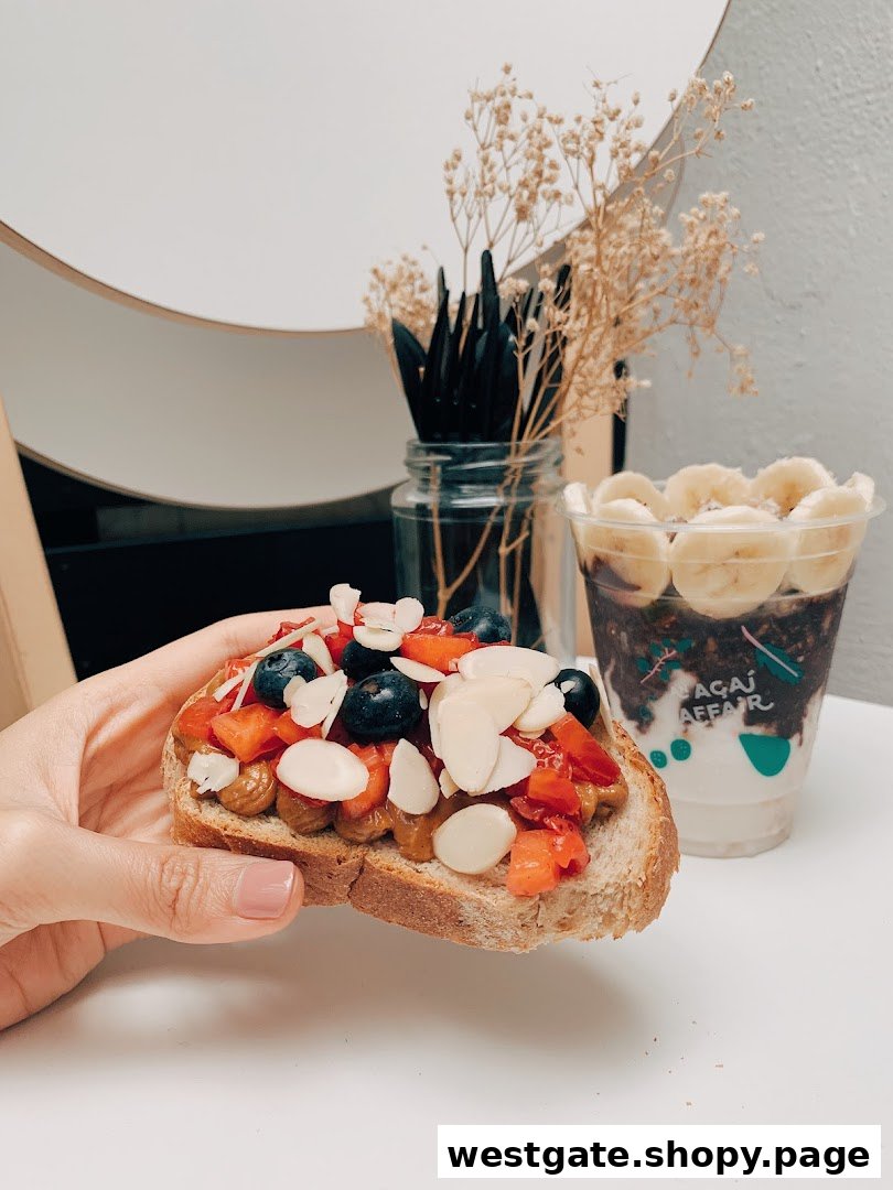 A hand holds a berry-topped toast next to an açaí bowl, showcasing fresh, healthy options.