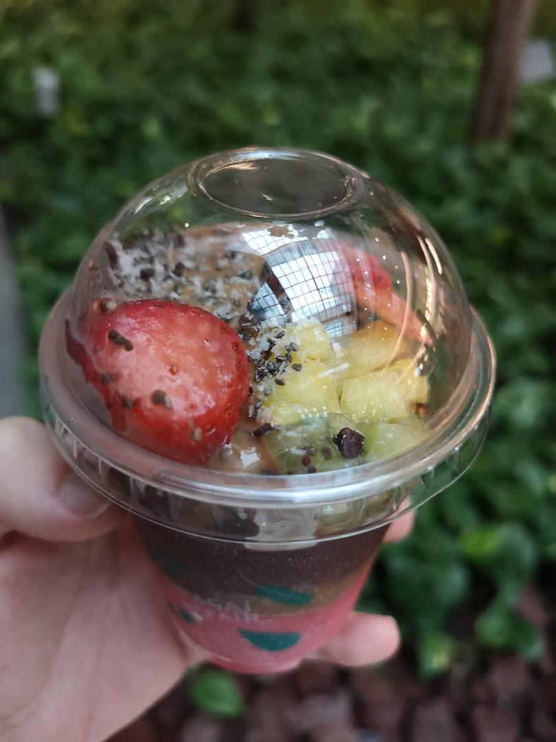 A hand holds a vibrant açaí bowl topped with fresh fruit, granola, and seeds.