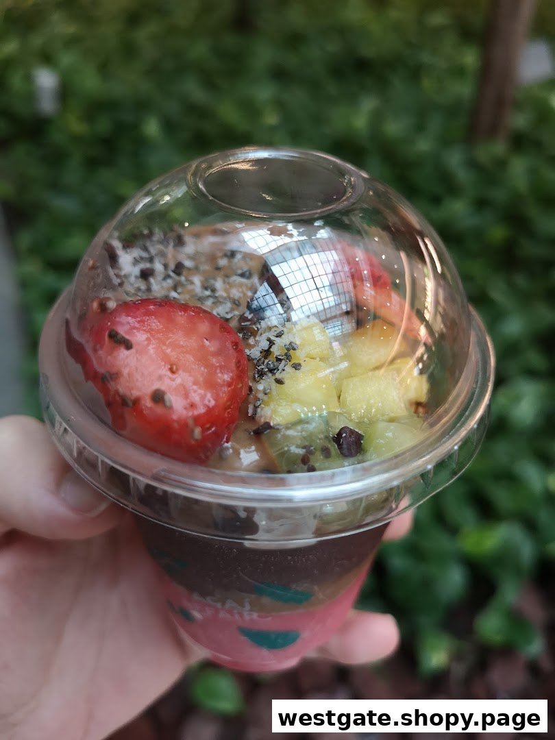 A hand holds a vibrant açaí bowl topped with fresh fruit, granola, and seeds.