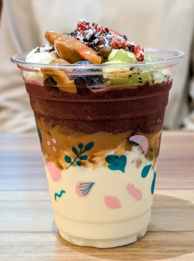 A vibrant açaí cup layered with fruit, nuts, and creamy bases, topped with fresh berries and kiwi.