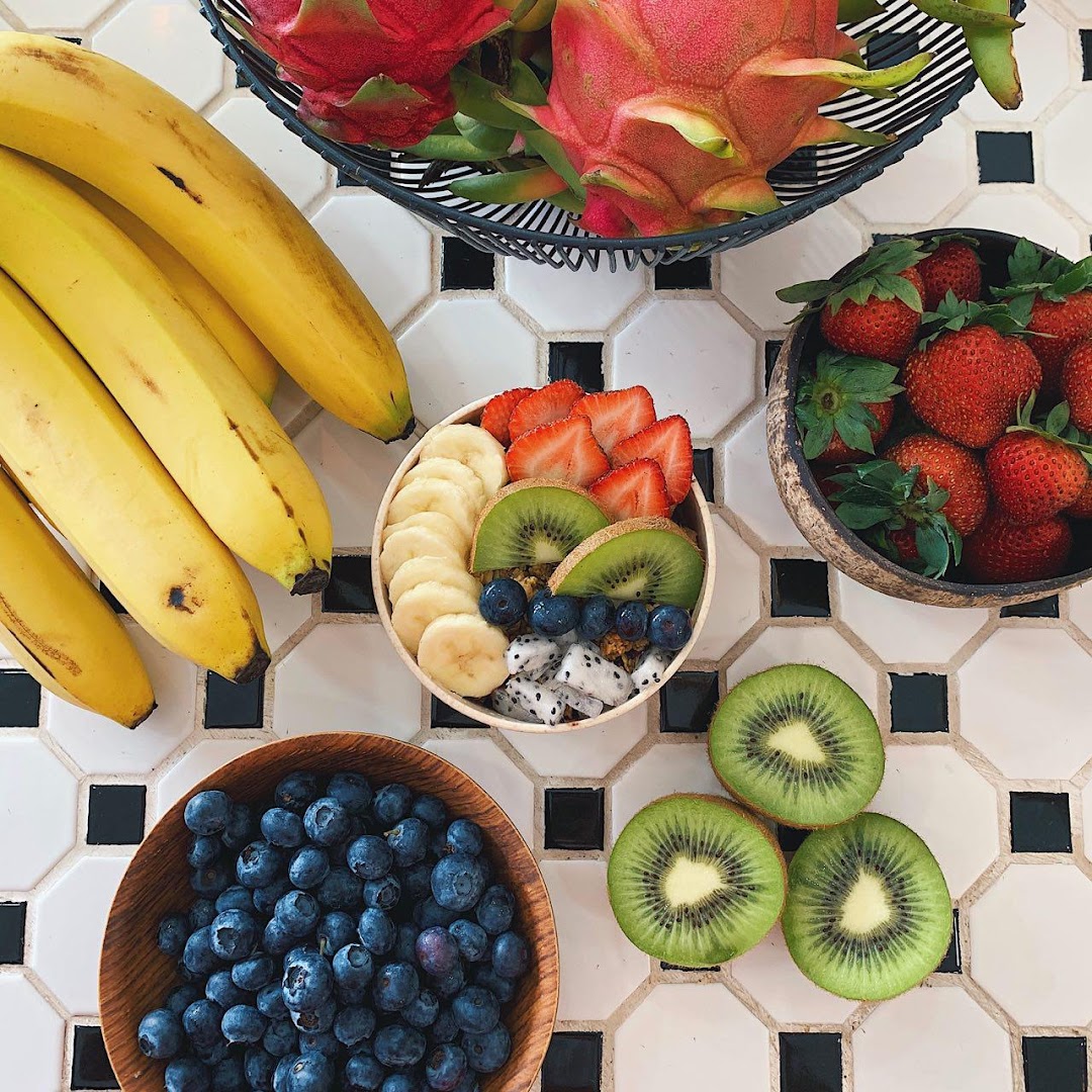 A vibrant açaí bowl surrounded by fresh bananas, strawberries, blueberries, kiwi, and dragon fruit.