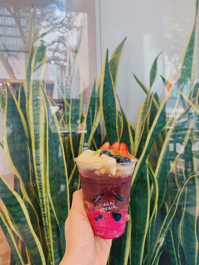 A hand holds a vibrant açaí bowl topped with fresh fruit and granola.