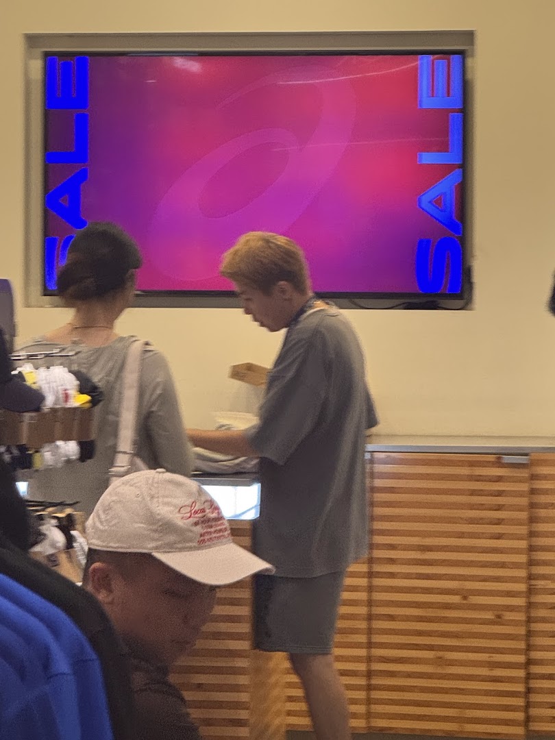Customers browsing inside an ASICS store with a large screen displaying a 'SALE' promotion and the ASICS logo.