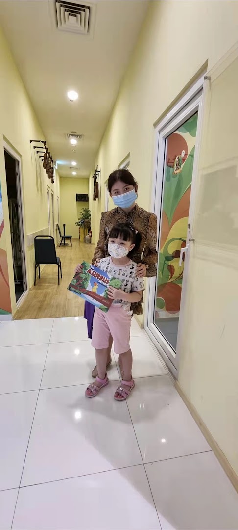 A woman and a child, both masked, stand in a bright hallway, likely within Aureus Academy.