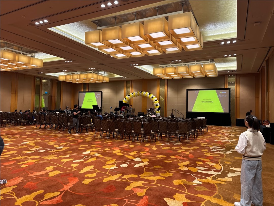 A large event hall with rows of chairs, two projection screens, and a stage, set up for a performance or presentation.