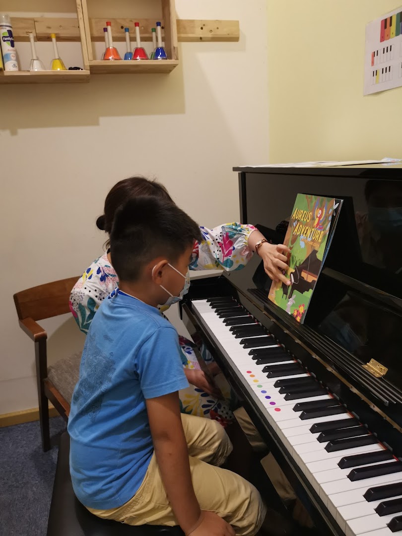 A teacher guides a student during a piano lesson at Aureus Academy, featuring musical instruments.