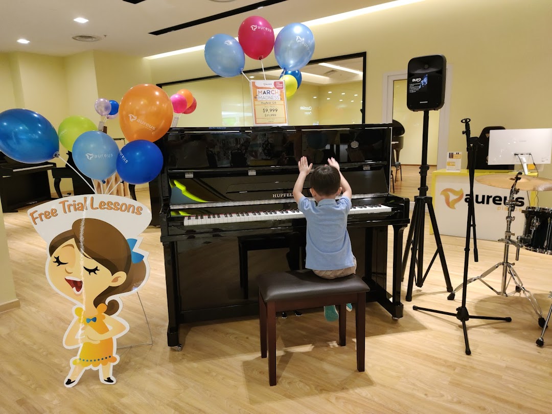 A child plays a piano inside Aureus Academy, surrounded by musical instruments and promotional balloons.