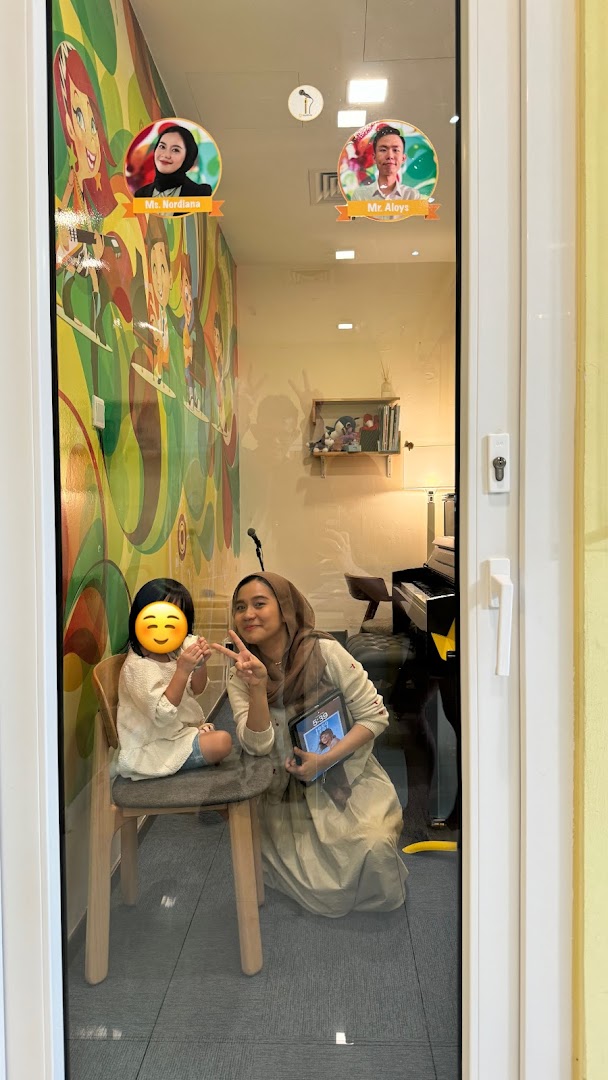 A teacher and student inside Aureus Academy, with colorful wall art and a piano visible.