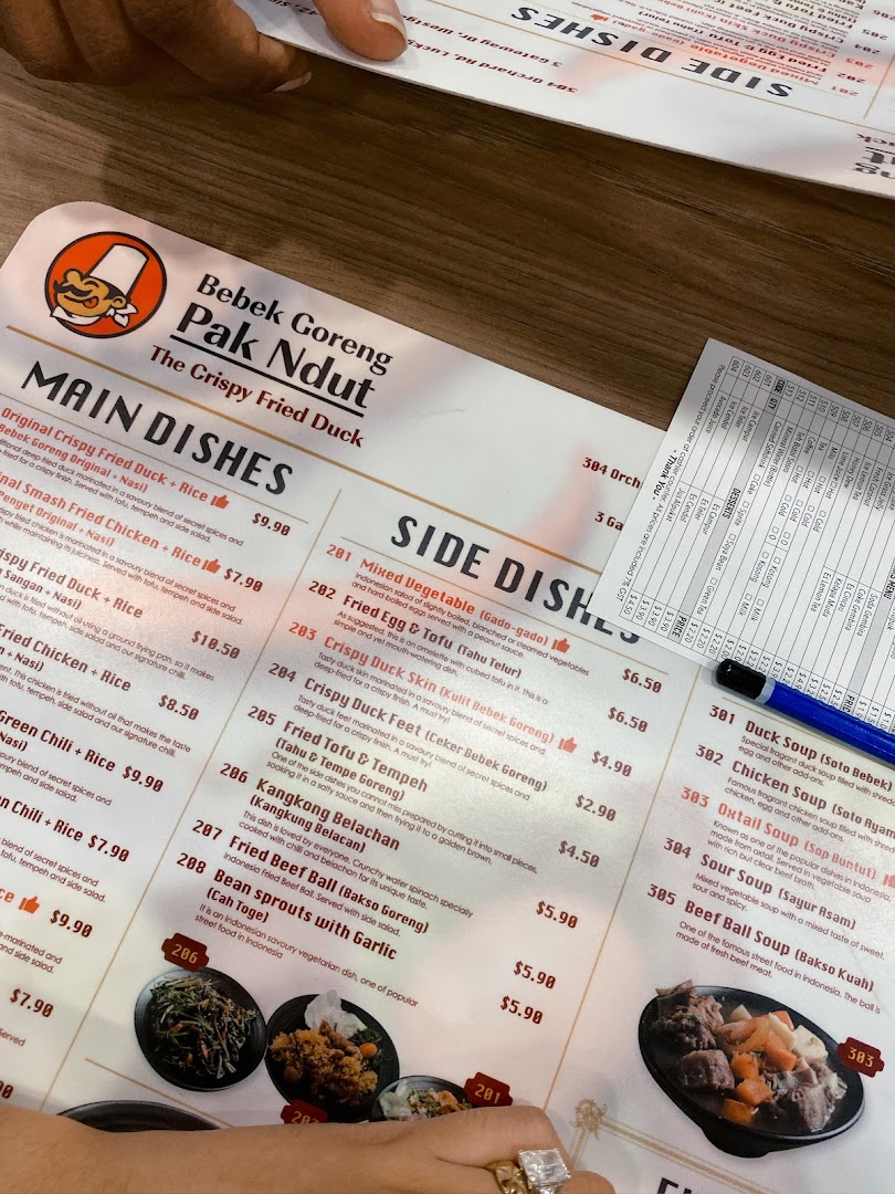 A close-up view of Bebek Goreng Pak Ndut's menu, featuring Indonesian main dishes, side dishes, soups, desserts, and drinks.