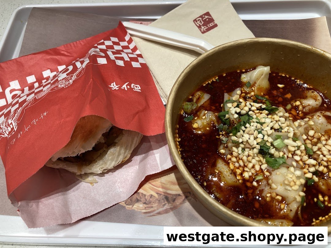A tray featuring a roujiamo (meat burger) in a red wrapper and a bowl of spicy wontons with peanuts.