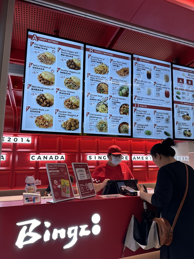 A customer orders at the counter of Bingz Singapore, with digital menu boards displaying various food and drink options.