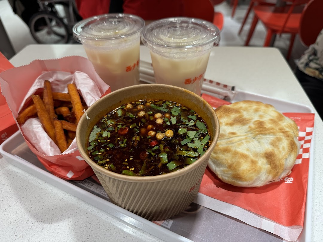 A tray featuring sweet potato fries, a spicy soup, a roujiamo bun, and two refreshing drinks.