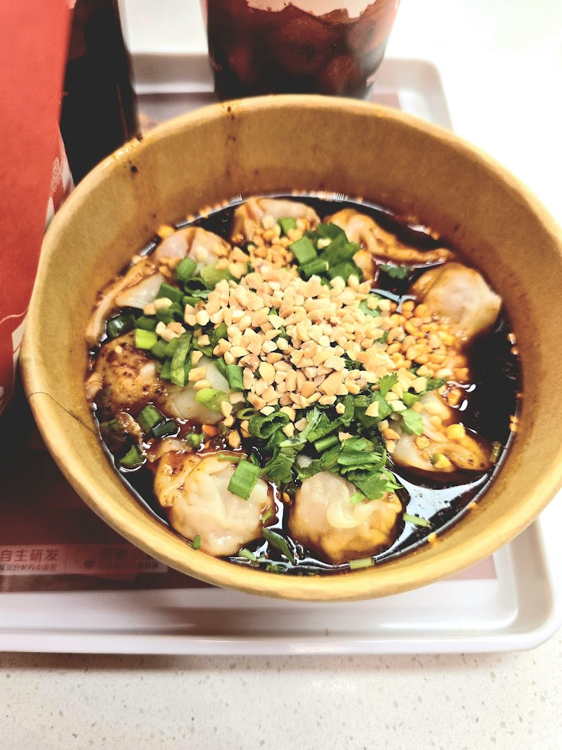 A close-up of a bowl of spicy dumplings topped with crushed peanuts and green onions.